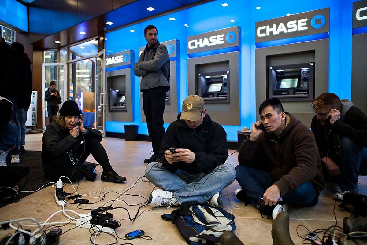 People crowd into a Chase Bank ATM kiosk to charge phones and laptops at 40th Street and 3rd Avenue, one block north of where power has gone out, on October 31, 2012 in New York, United States. "This is the modern campfire," one man mentioned to another man. Businesses across the eastern seaboard are attempting to return to normal operations as clean-up from Hurricane Sandy continues. (Photo by Andrew Burton/Getty Images)