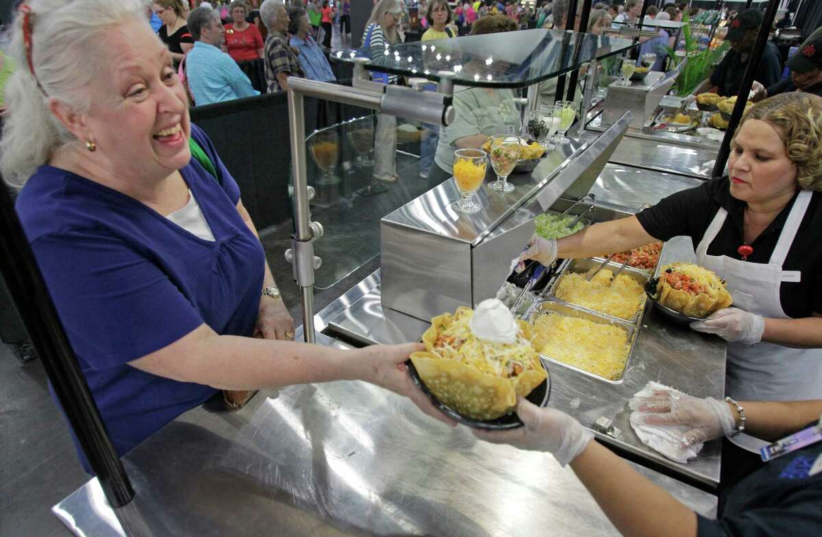 Suzanne Lindsay, left, of Ft. Lauderdale picks up her taco salad as worker Judy Delgado, right, prepares another salad in the food court during the International Quilt Festival at the George R Brown Convention Center, 1001 Avenida de las Americas, Thursday, Nov. 1, 2012, in Houston. The food court is filled with options including new items of a cupcake truck and a grilled cheese station. Each year, the food court serves more than 8,000 baked potatoes and 7,000 taco salads.