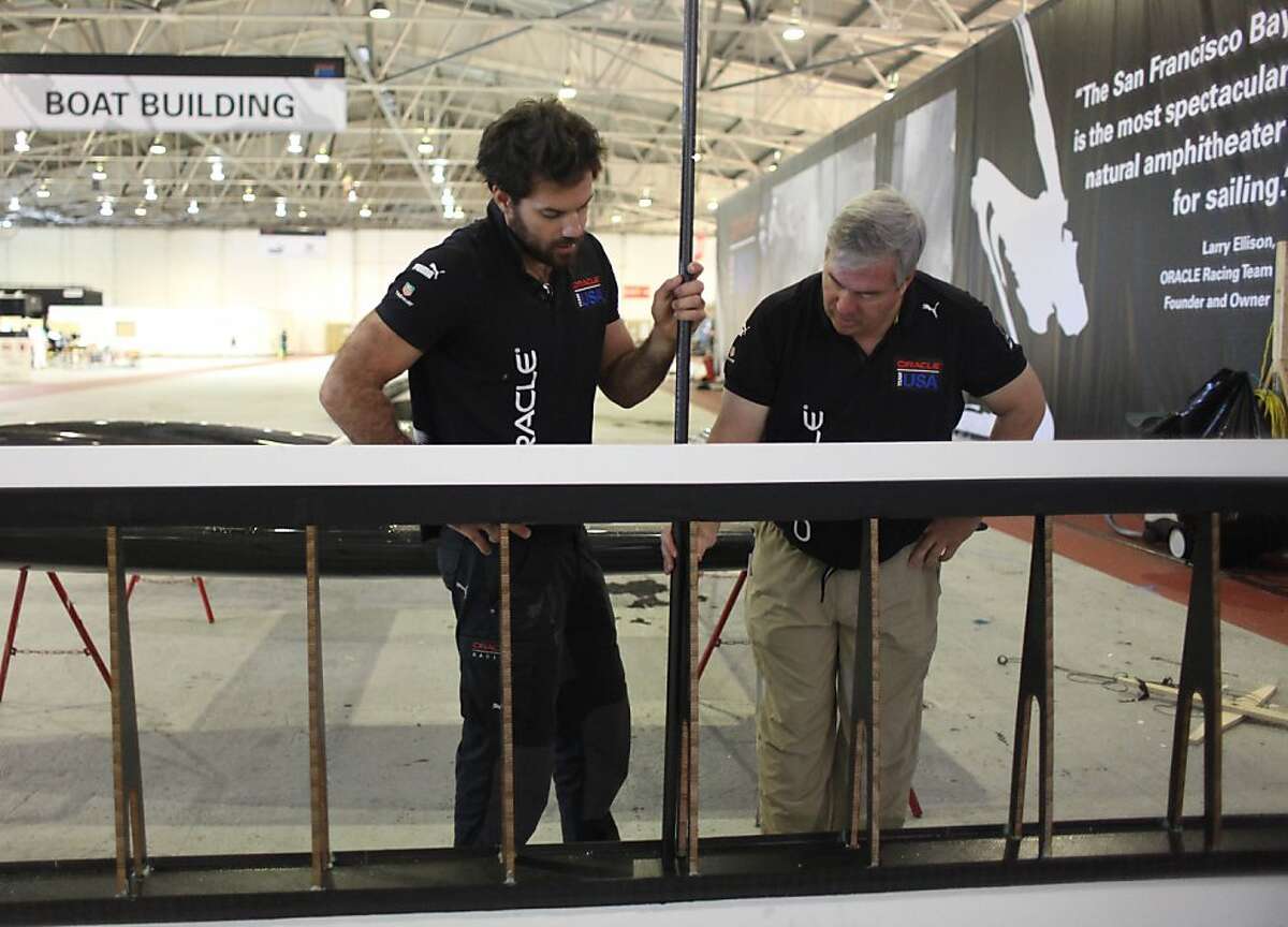 Shannon Falcone (l to r), Oracle Team USA sailing team member, and Tom Speer, Oracle Team USA Aero & Sail Project Leader, stand behind part of a wing salvaged from the Oracle Team USA AC72 boat, which capsized on October 16, 2012, as they discuss the construction of a flying machine for Red Bull Flugtag San Francisco 2012 at the team base on Monday, November 5, 2012 in San Francisco, Calif. The part of the wing salvaged off the AC72 boat will be used on the flying machine being constructed.
