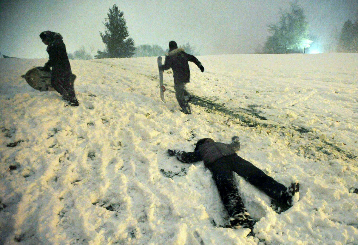 Kai Baldwin, 10, foreground, makes a snow angel, and James Lema, 12, left, and Javen Duff, 11, climb the hill in front of Immaculate High School with their snowboards during the first snowfall of the season.