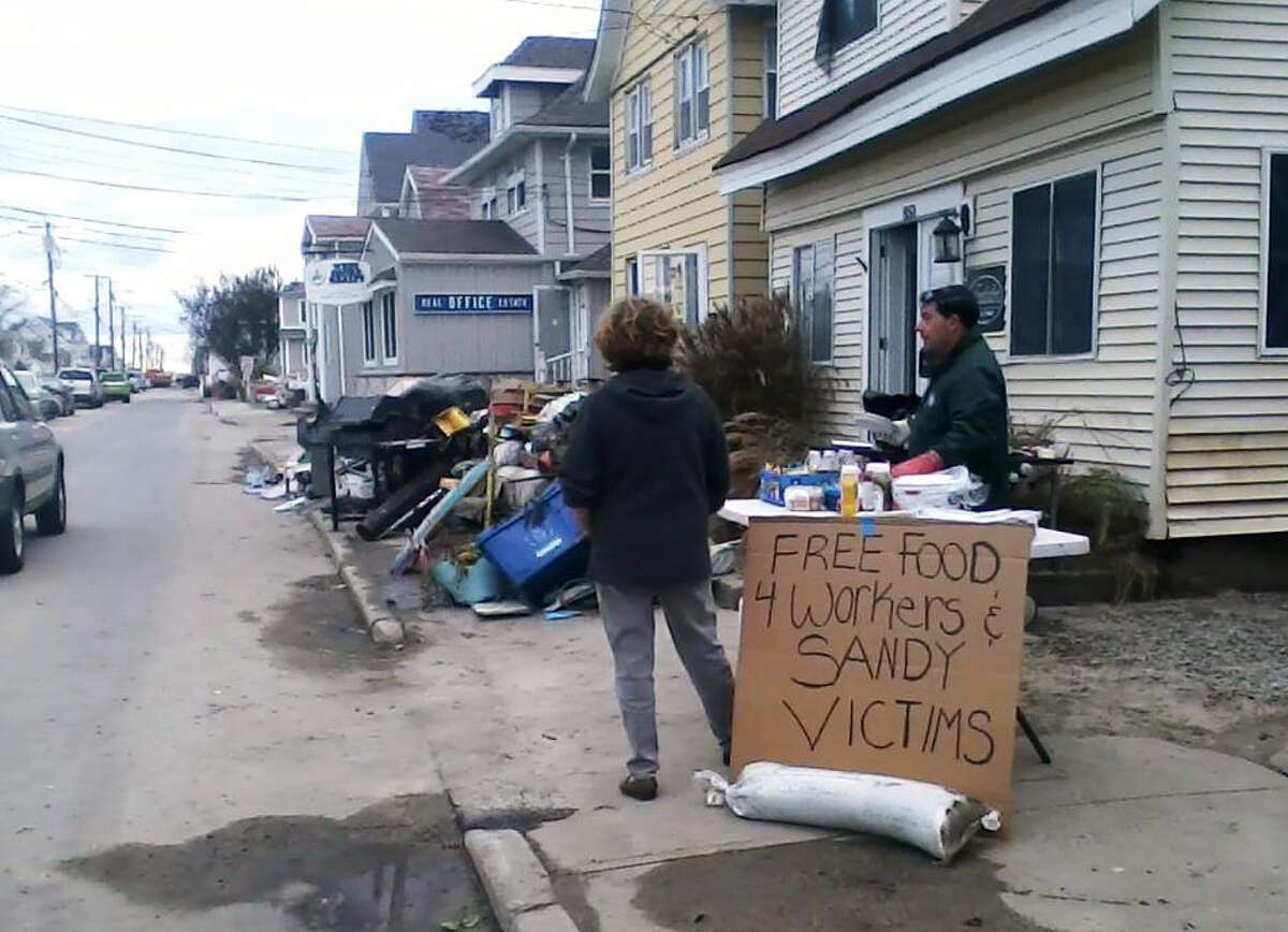 Carl Loschiavo, owner of the house shown behind him on East Broadway in Milford, took to a grill on Friday and Saturday after the passing of Hurricane Sandy to cook hot dogs and hamburgers for residents and emergency workers.