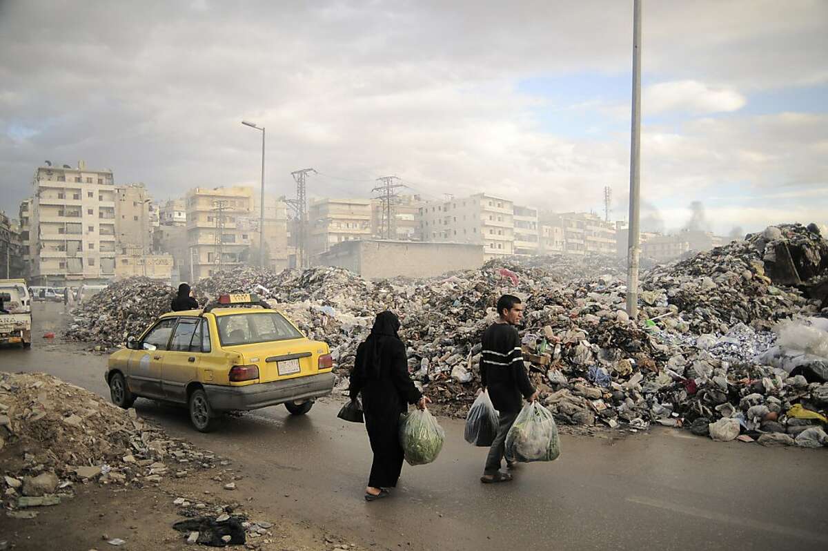 In this Saturday, Nov. 10, 2012 photo, Syrians carry their rubbish to a mountain of garbage in a roundabout in Aleppo, Syria. Due the heavy fighting and shelling, the garbage collection system collapsed weeks ago. (AP Photo/Mónica G. Prieto)