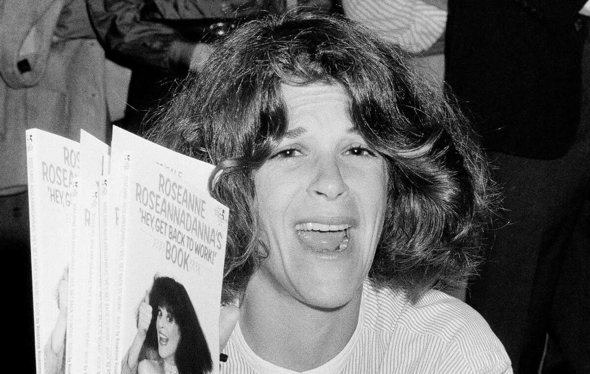 FILE - In this Sept. 27, 1983 file photo, actress and comedienne Gilda Radner holds up copies of her book, "Roseanne Roseannadanna's "Hey, Get Back To Work," at a New York bookstore. The Madison, Wis.-area chapter of Gilda's Club is the latest to change its name to the Cancer Support Community, a move its director said was necessary because young people don't know who Radner was. (AP Photo/Suzanne Vlamis)
