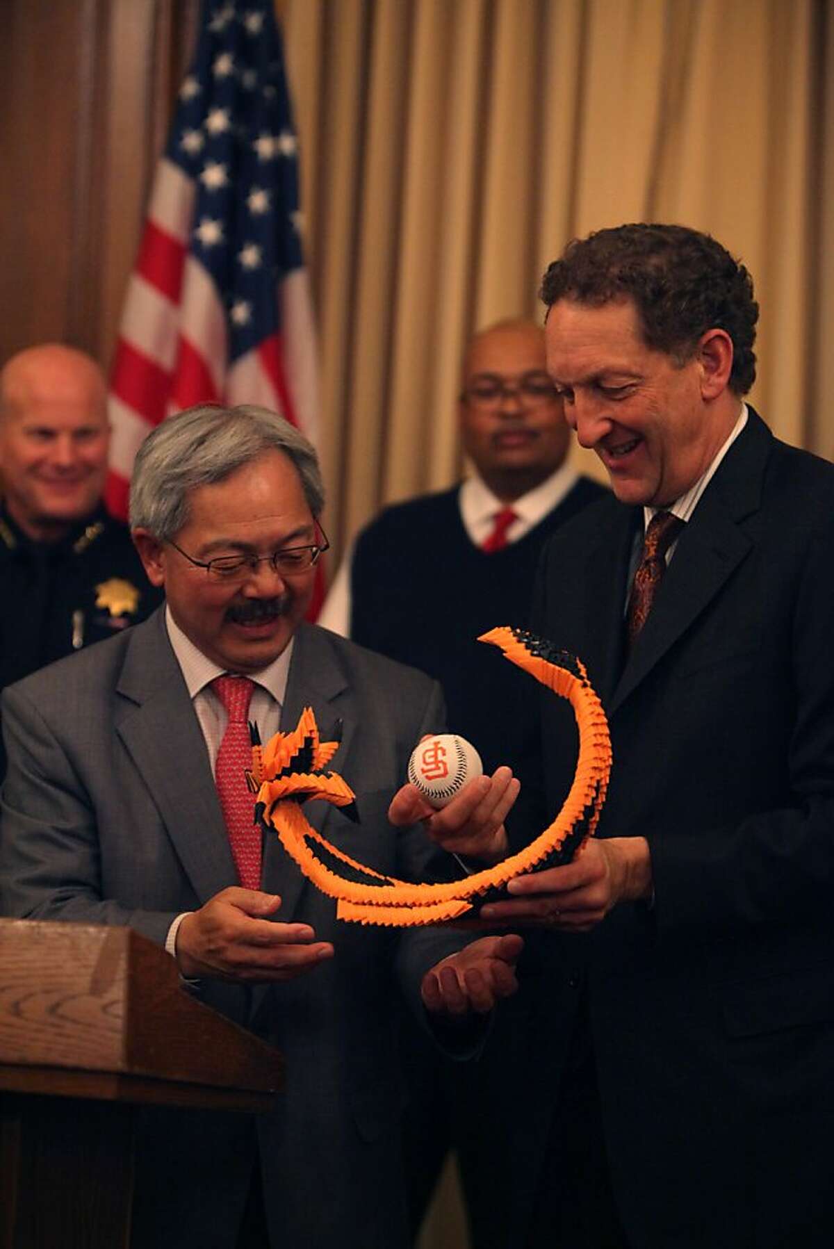 Mayor Ed Lee (l to r) stands with Giants CEO Larry Baer as Baer holds a paper dragon carrying a World Series ball presented to him during a press conference regarding the World Series Championship Parade and Civic Celebration at the Mayor's Office on Tuesday, October 30, 2012 in San Francisco, Calif.