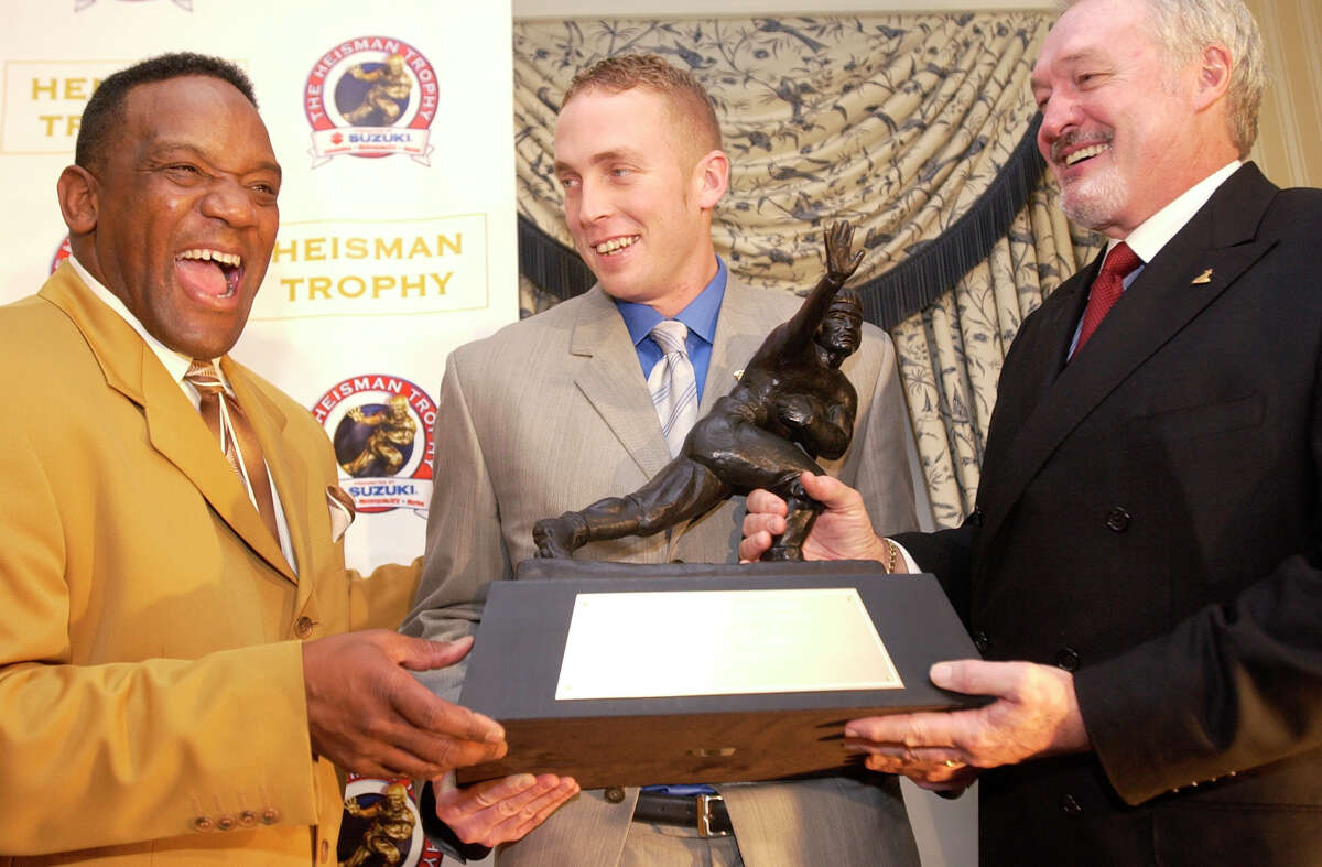 Heisman Trophy winner Jason White, center, a quarterback from Oklahoma, holds the Heisman Trophy with former Oklahoma Heisman Trophy winners Billy Sims (1978), left, and Steve Owens (1969) at the Yale Club in New York Saturday, Dec. 13, 2003. White is  a native of Tuttle, Okla., population 6,019 as of the 2010 Census and Sims is a native of Hooks, population 2,973 in 2010.