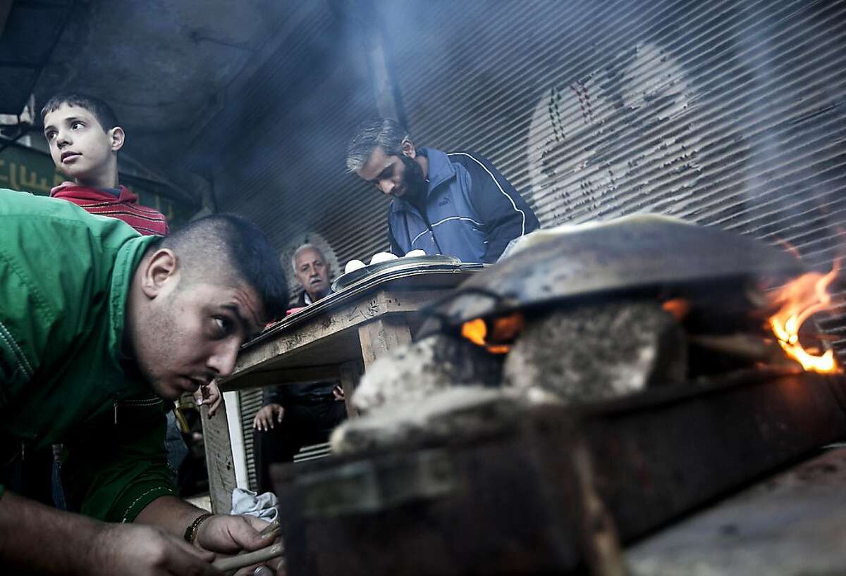 A man makes bread as residents, background, stand in line in front of a bakery during heavy fighting between Free Syrian Army fighters and government forces in Aleppo, Syria, Tuesday, Dec. 4, 2012. (AP Photo/Narciso Contreras)