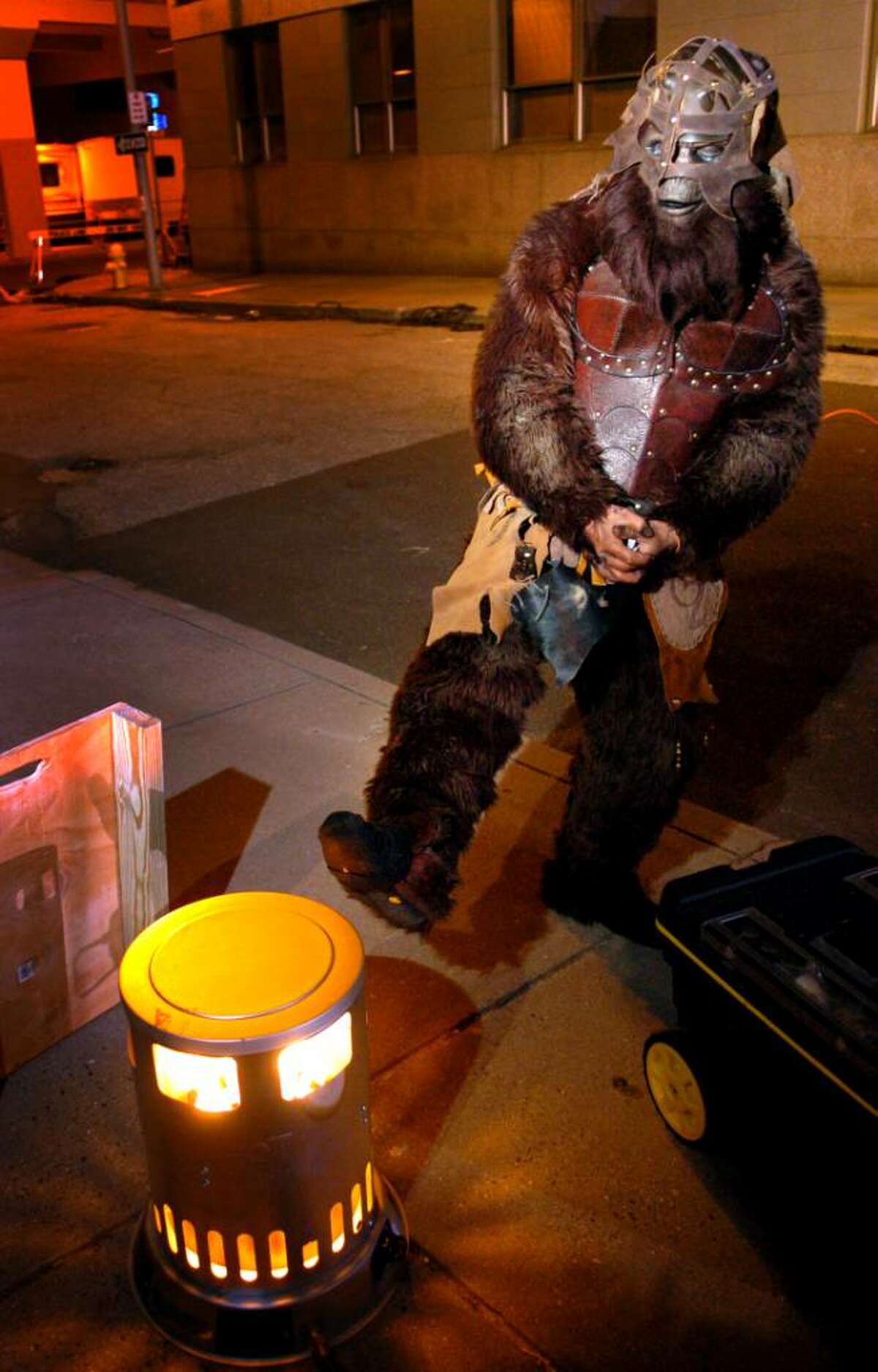 A monkey from "The Witches of Oz" warms his feet between takes Thursday evening in downtown Bridgeport.