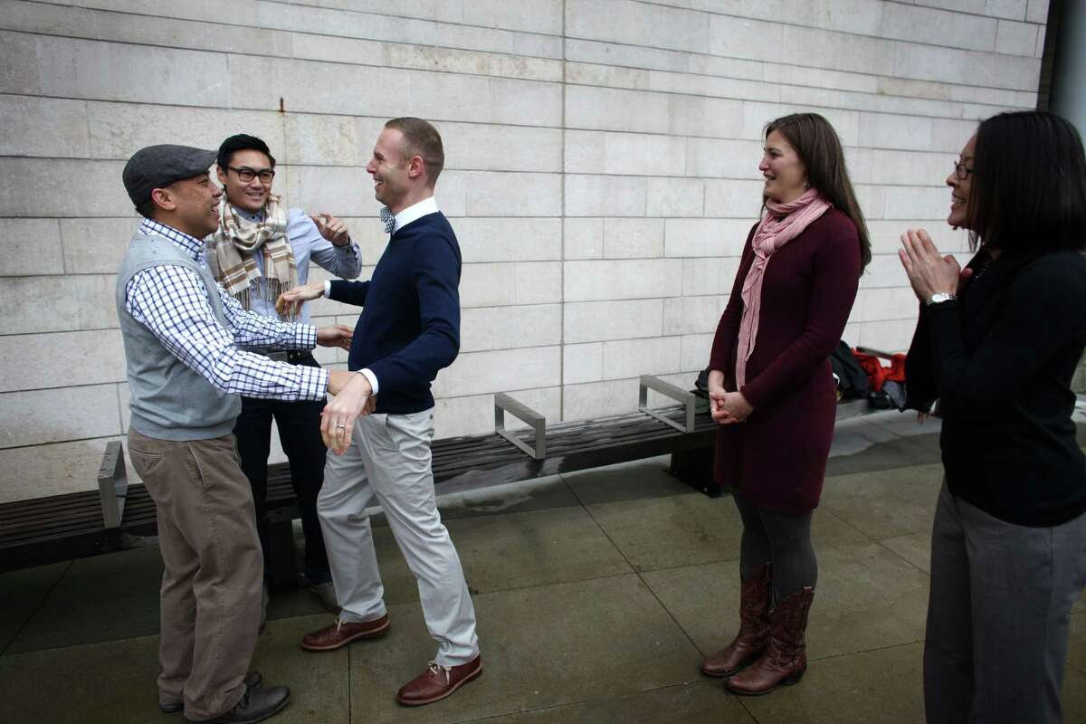 Bernie Liang, left, and his husband Ryan Hamachek prepare to kiss as they are married by Paolo Campbell outside of Seattle City Hall. Liang and Hamachek tried to get a slot in the official City Hall weddings but were unable so they decided to just get married outside. "We flash mobbed the wedding ceremonies," said Liang. They have been together for 8 years. At right are witnesses Megan Garner and Monica Nixon, far right.