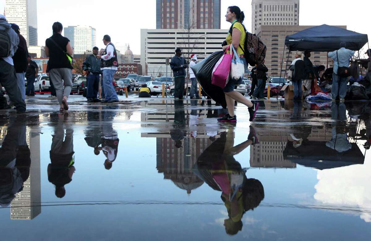 Evelyn Anness is reflected in puddles left by a passing storm as she walks with her arms full of items and free clothing at the Extended Aftercare Alumni holiday event in downtown Houston. Volunteers distributed a holiday meal, clothes, and hygiene gift packages on Christmas morning.