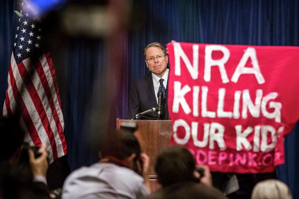 An activist with Code Pink interrupts Wayne LaPierre, executive vice president of the National Rifle Association, during a news conference held to address the Newtown, Conn., mass shooting, in Washington, Dec. 21, 2012. During the news conference Friday, the NRA called for armed protection for each school in the country as the best way to protect children from gun violence.