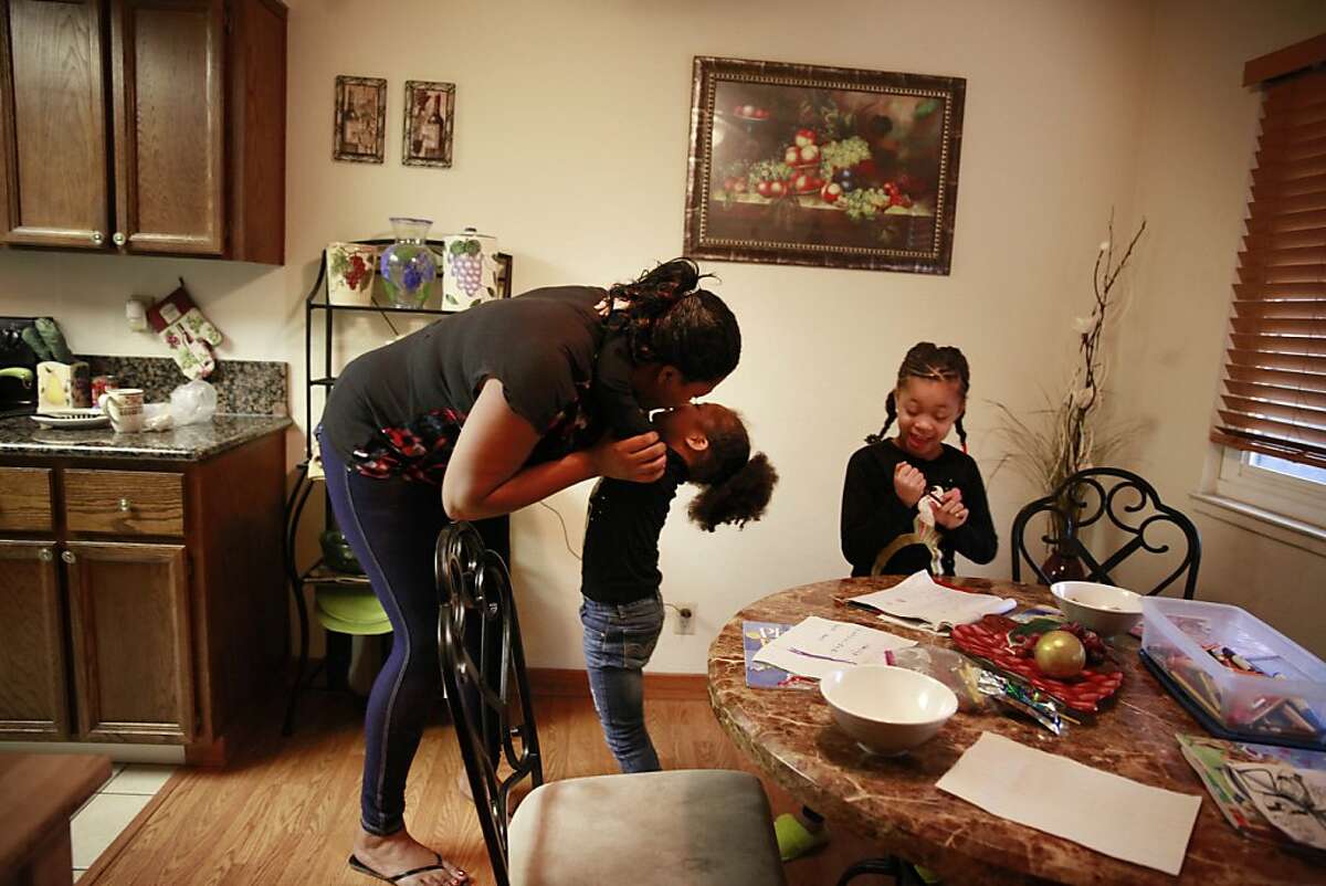 Latifa Lewis (left) gets a hug from her daughter Taylor Lewis (center), 4, after arriving back at home after looking at an apartment for rent as Kamil Lewis (right), 5, works on her writing at the dinning table on Wednesday, January 23, 2013 in Hayward, Calif.