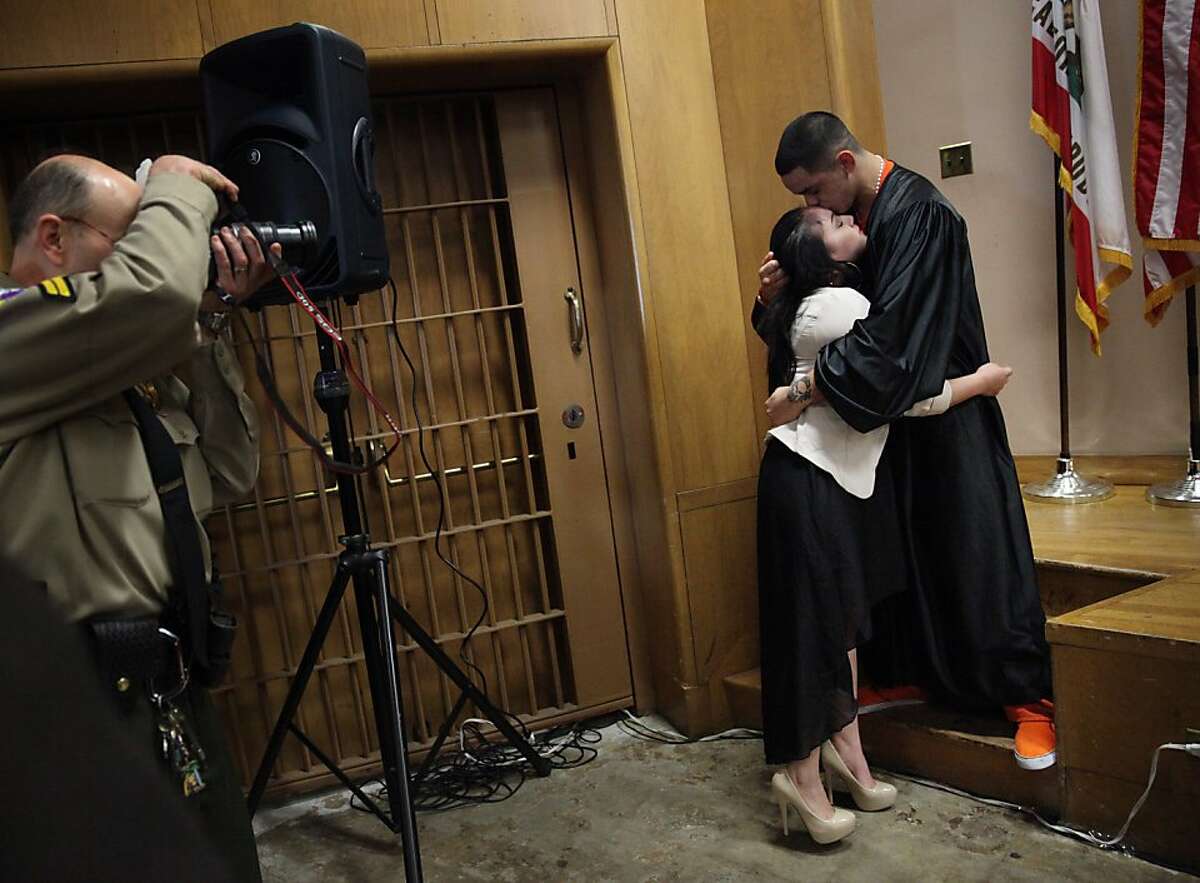 Mayte Lopez (second from right) and Kristopher Viana (right) hug after Viana received his diploma during the San Francisco Sheriff Department's Five Keys Charter School graduation ceremony as Mike Gunn (left), senior deputy, takes photographs during a portrait opportunity with friends and family in the Hall of Justice 6th floor auditorium on Tuesday, January 29, 2013 in San Francisco, Calif.