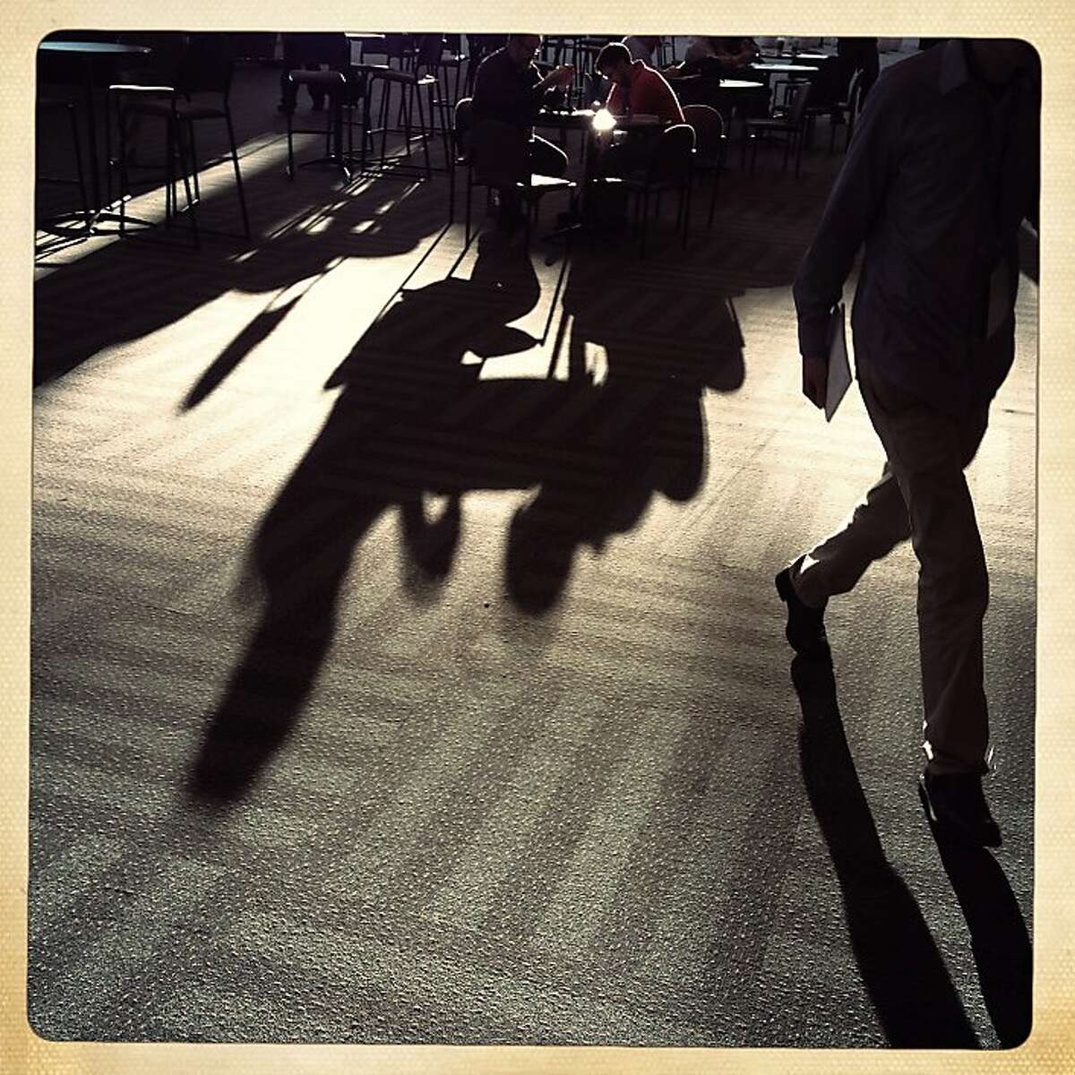 The shadows of Brad Johnson (l to r) and Issac Johnson, both of Burnsville, Minnesota, are cast across the second floor of Moscone Center West in the morning during Macworld/iWorld as the father and son work at a table on Thursday, January 31, 2013 in San Francisco, Calif.