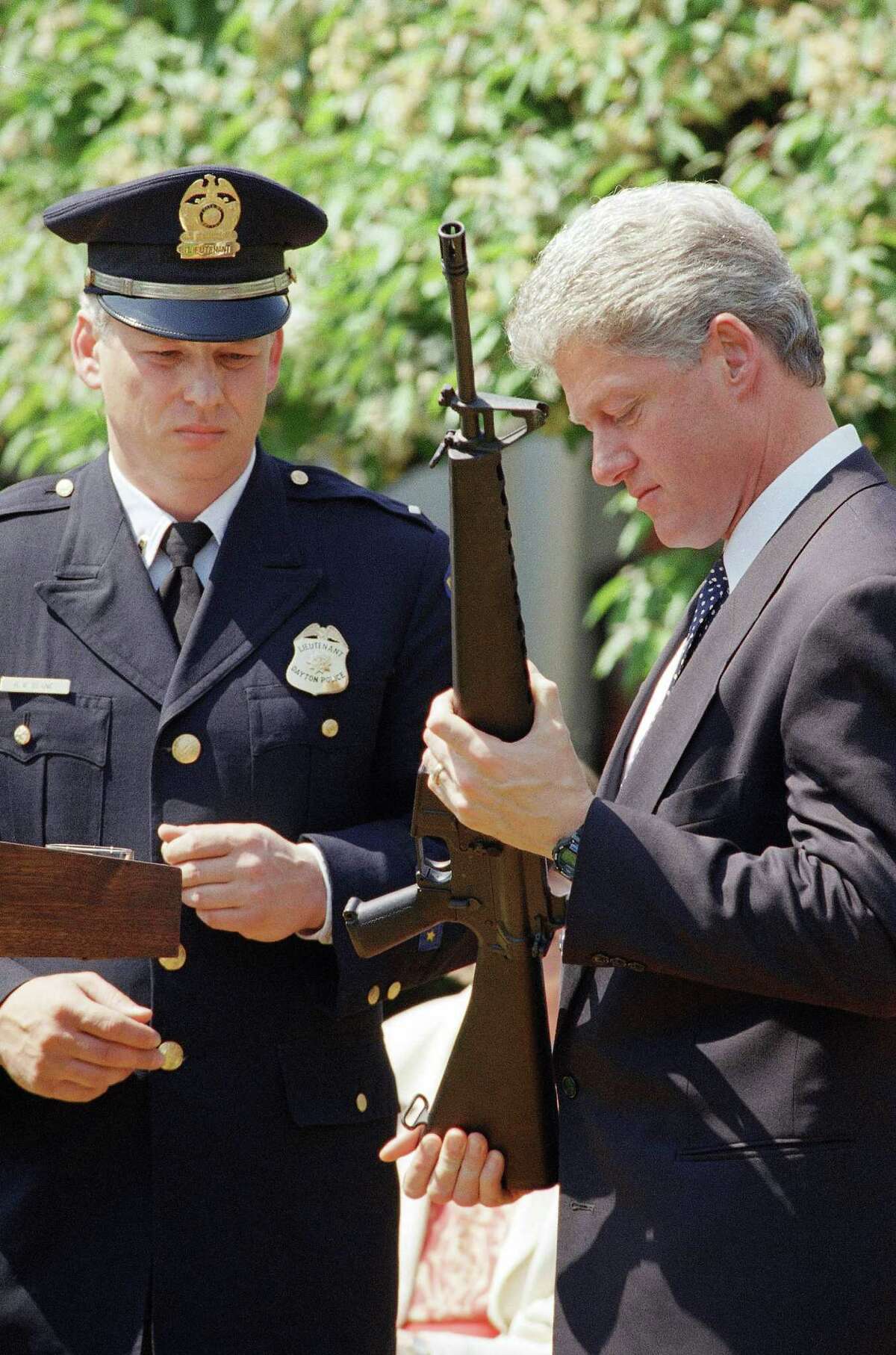 FILE - In this April 25, 1994 file photo, President Bill Clinton holds a Colt AR-15 rifle during a ceremony in the Rose Garden of the White House in Washington, where he launched efforts to pass the assault weapons ban. Dayton, Ohio Police Lt. Randy Bean, whose fellow officer Steve Whalen was gunned down with an AR-15 in 1991, looks on at left. The White House has released a photo of President Barack Obama firing a gun, two days before he is set to travel to Minnesota to discuss gun control. It shows Obama shooting at clay targets on the range at Camp David, the presidential retreat in Maryland, where he says he engages in the sport "all the time." The image was released at a time when Obama is pushing a package of gun-control measures in response to the Newtown, Conn., school shooting. But the image of a U.S. president holding a gun is certainly nothing new. (AP Photo/Dennis Cook, File)