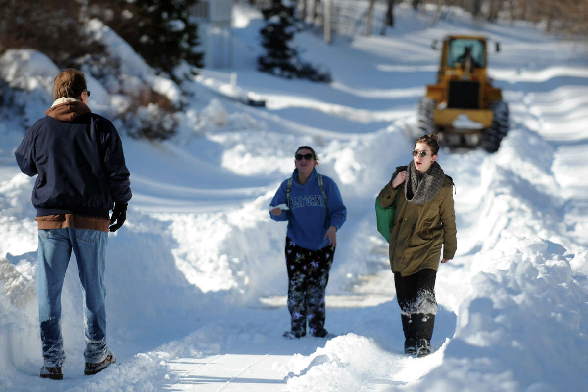 Pedestrians walk in the wake of a tractor as it make the first trip to clear snow from the north section of Cutspring Rd., in Stratford, Conn., Feb. 10th, 2013.