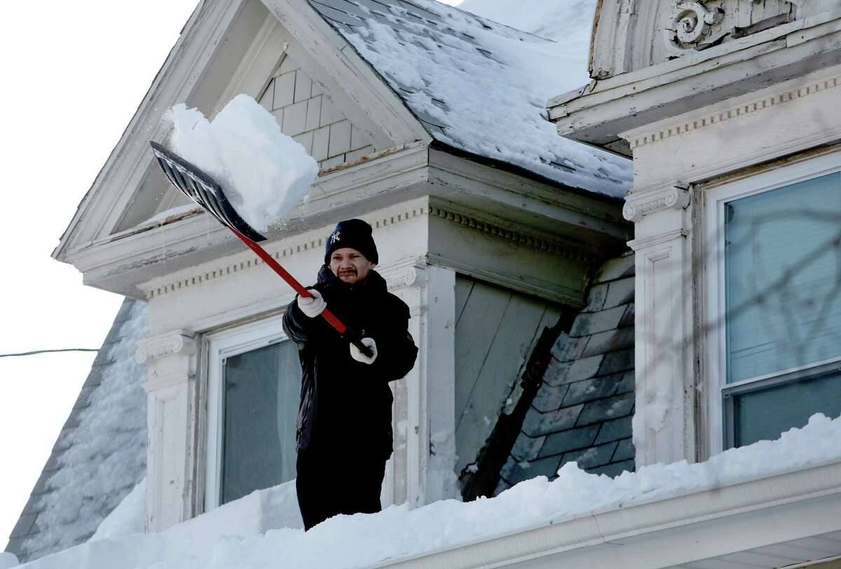 Noe Rodriguez works to remove snow of the roof of his home on the 1400 block of Noble Ave. in Bridgeport, Conn. on Sunday Feb. 10, 2013. Residents were still working to dig themselves out from the weekend blizzard.