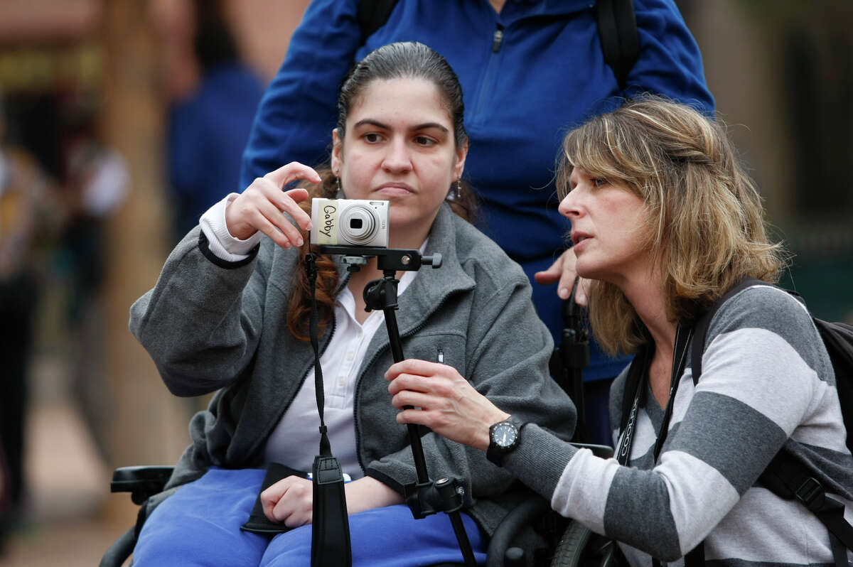 Workshop organizer, Courtney Bent, right, teaches Gabrielle Howard, 29, how to use a camera that is attached to her wheelchair as a group of special needs adults participates in a photo shoot at the Houston Zoo.