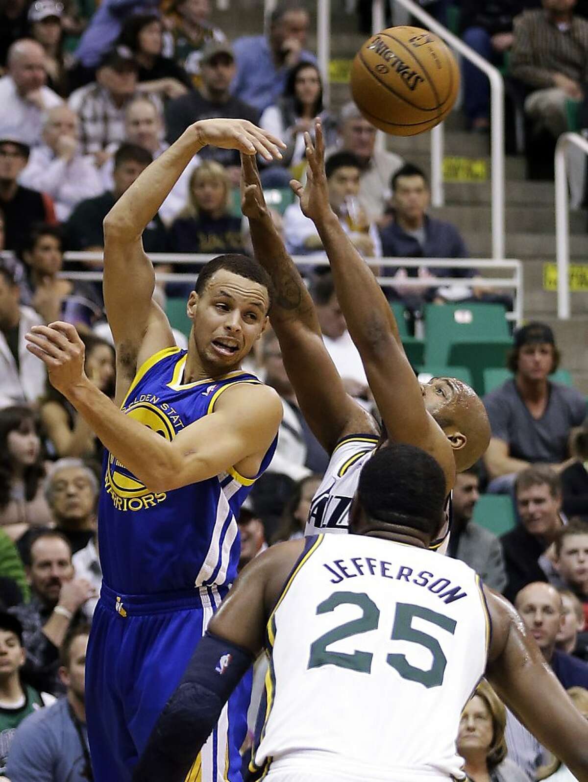 Golden State Warriors' Stephen Curry, left, passes the ball as Utah Jazz's Jamaal Tinsley, rear, defends in the first quarter during an NBA basketball game Tuesday, Feb. 19, 2013, in Salt Lake City. Jazz's Al Jefferson (25) watches the play. (AP Photo/Rick Bowmer)