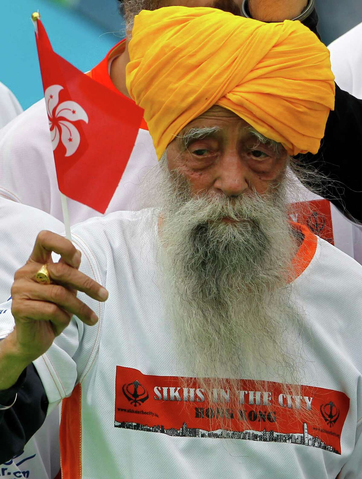 Centenarian marathon runner Fauja Singh, 101, center, originally from Beas Pind, in Jalandhar, India but who now lives in London, raises a Hong Kong flag after finishing a 10-kilometer race, which was part of the annual Hong Kong Marathon, in Hong Kong Sunday, Feb. 24, 2013. Singh will retire from public racing after competing in the marathon.