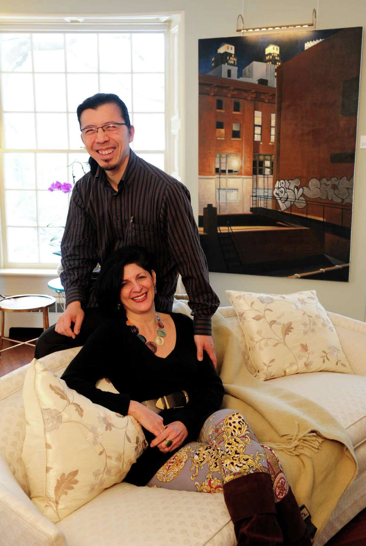 Jeanine Esposito and husband Frederic Chiu sit in front an oil painting by Duvian Montoya, "A New York Light," at their Westport home Tuesday, Feb. 26, 2013. The couple hosts art events in their home called Arts Immersion Salons, through their non-profit organization, Beechwood Arts.