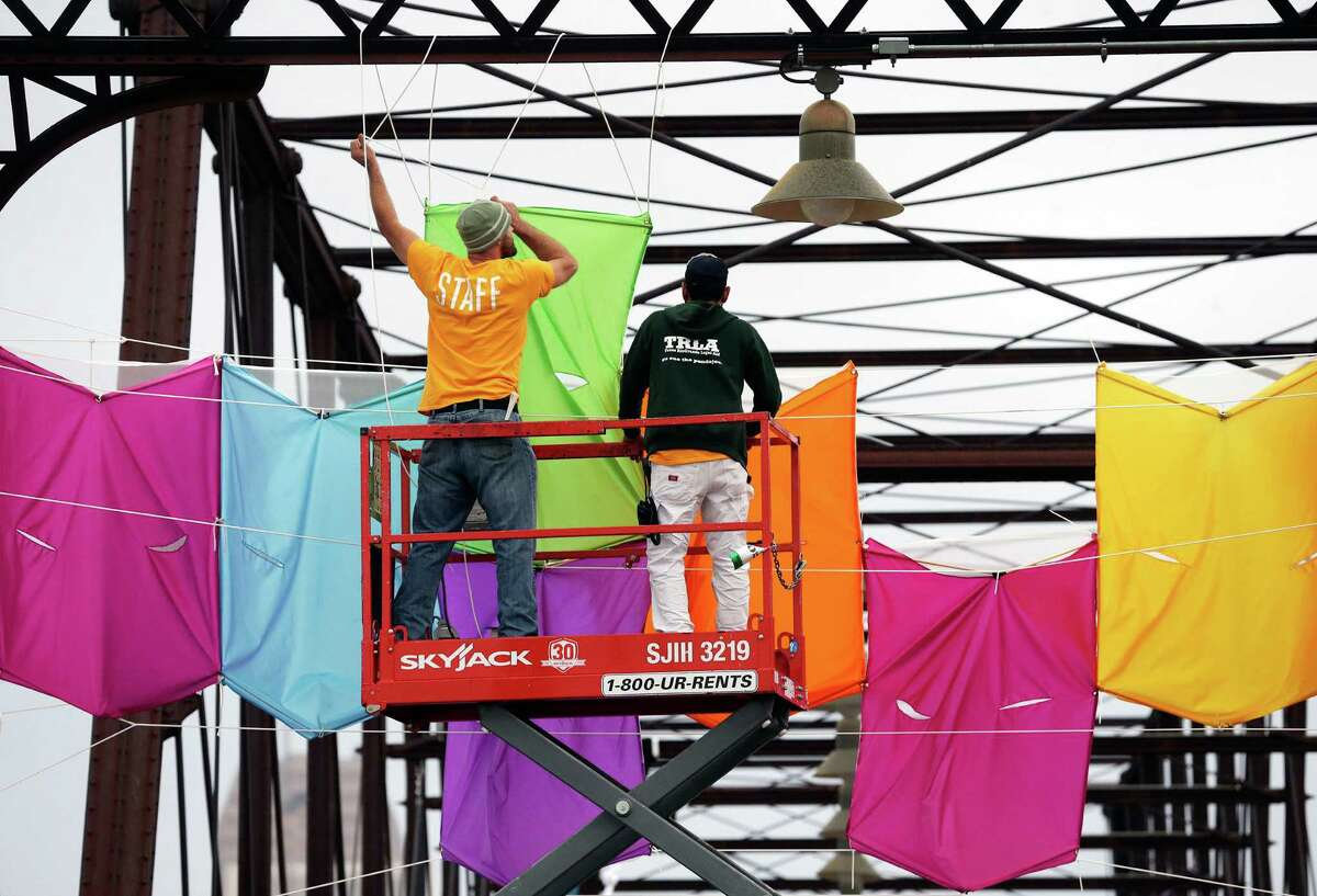 Reagan Johns (left) and Ed Saavedra hang material which will featured with lighting as Luminaria production workers work on hanging hardware for a display on the Hays Street Bridge on November 9, 2016.