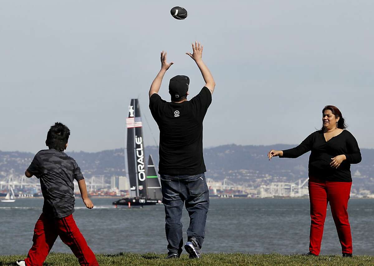 The Macedo family, Isaac (left), Benny and Annie played some touch football in the small park next to McCovey Cove near AT&T park while an Oracle racing vessel practiced in the bay. No rain and a week of spring fever is prompting many in San Francisco, Calif. to spend their lunch hours outside Monday March 11, 2013.