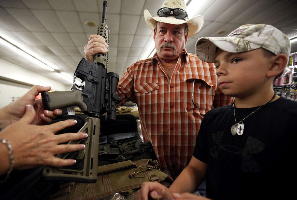 Johnny Hickman and son Jake, 10, of Midland listen to Connie Whiting of Five Four Tactical explain how an AR-15 has been customized at the Sweetwater Gun, Knife and Coin Show in Odessa on Saturday.
