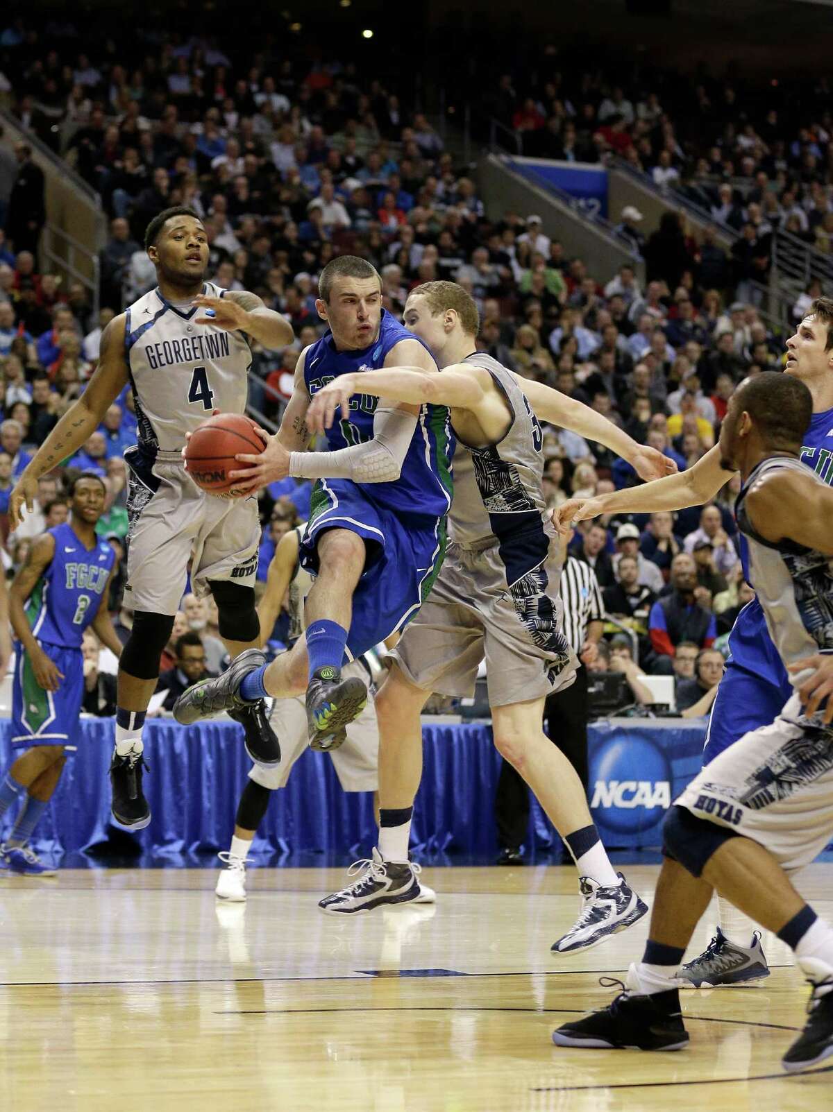 Brett Comer #0 of the Florida Gulf Coast Eagles looks to pass the ball in the second half as he drives against Nate Lubick #34 and D'Vauntes Smith-Rivera #4 of the Georgetown Hoyas during the second round.
