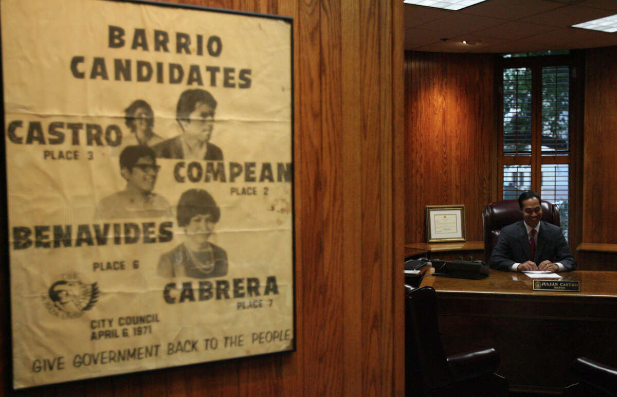 Julian Castro sits in his new office at City Hall. The poster, left, has a 1971 photo of his mother from her campaign with the Committee for Barrio Betterment.
