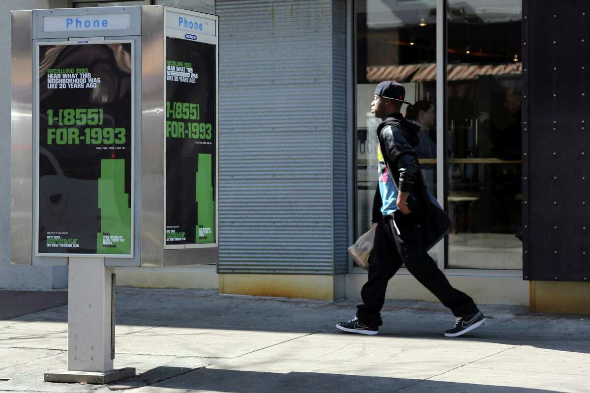 In this Friday, April 5, 2013 photo, a pedestrian walks past a pay phone advertising the New Museum's "NYC 1993: Experimental Jet Set, Trash and No Star" exhibit. The New Museum has launched an exhibit called "NYC 1993,Ã‚Â” which fills five floors with works by more than 75 different artists. But the interesting part is how they've taken their show to the streets, with 5,000 payphones outfitted with stickers that say "1-855-FOR-1993."