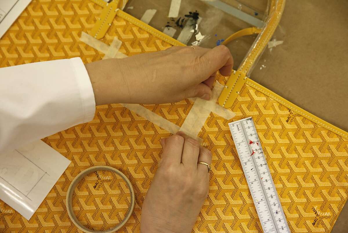 Goyard artist Christine Mendez tapes down an area where she will be laying a stencil to paint a monogram onto a Goyard handbag at the Goyard atelier on Tuesday, March 19, 2013 in San Francisco, Calif.