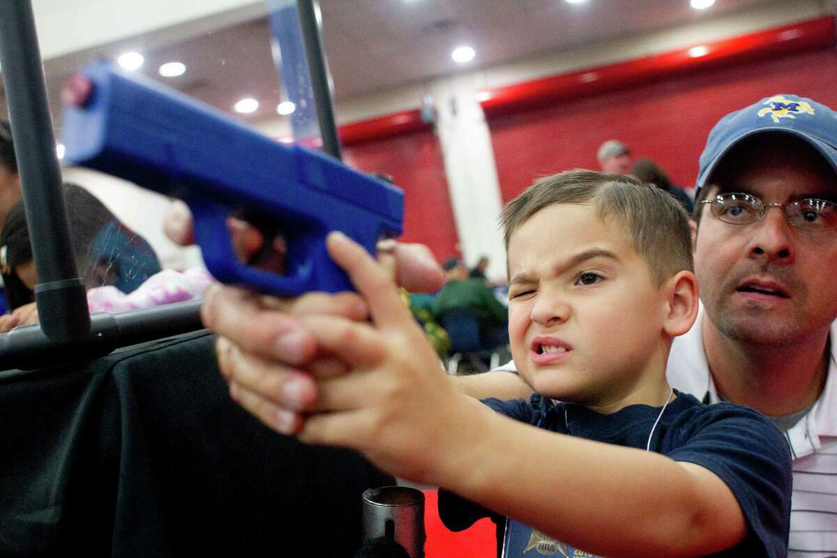 Heath Bryant of Cypress assists his son, Tate, 5, to shoot a target using a video game-style of gun at an exhibit booth during NRA Youth Day events at the National Rifle Association's 142 Annual Meetings and Exhibits in the George R. Brown Convention Center Sunday, May 5, 2013, in Houston. More than 70,000 are expected to attend the event with more than 500 exhibitors represented.