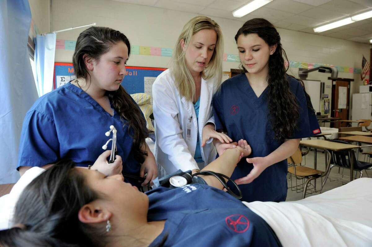 Katie Tong, center, a registered nurse and certified teacher at Danbury High School, works with students in her class Monday, May 13, 2013. At right, Christie Colucci, 18, and Rebeca Eller, left, also 18, learn to take blood pressure. Jennifer Avila, 16, acts as the patient.