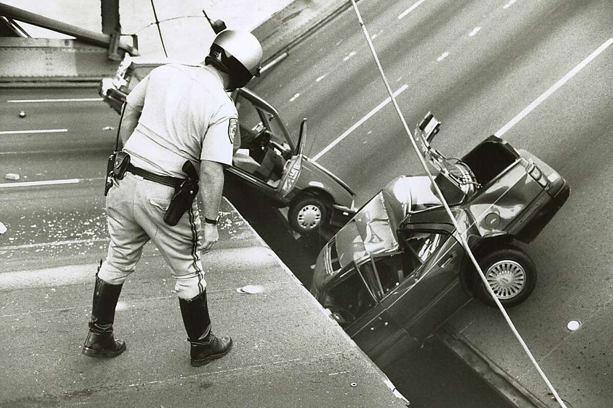 A CHP officer checks the damage to cars that fell when the upper deck of the Bay Bridge collapsed onto the lower deck on October 17, 1989. Loma Prieta Earthquake.