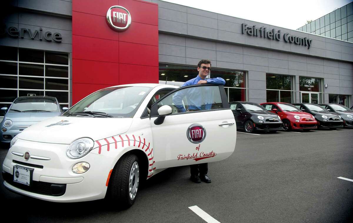 Intern Evan Costa poses for a photo with a Fiat 500 POP at Callari Fiat in Stamford, Conn., decorated in a baseball design for display at a Bluefish game and the Cooperstown Classic golf tournament.