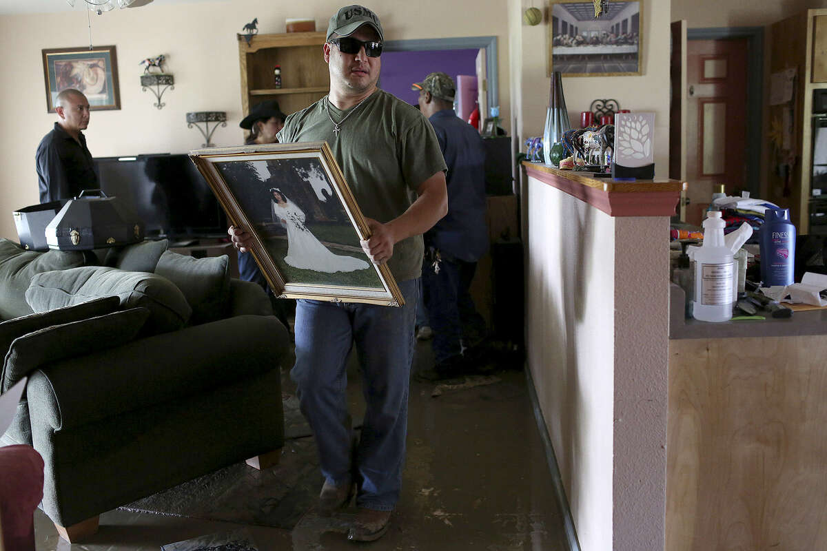 Anthony Wilfong carries Celia Olivarez's wedding portrait out of her home, which was flooded with several feet of water on Espada Road. The wedding picture was taken at nearby Mission Espada and was undamaged by the flood.