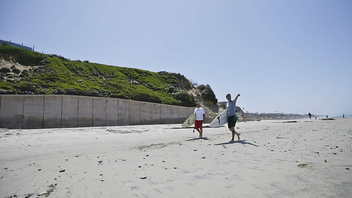Surfers walk the sand in Solana Beach, Calif., Monday, May 20, 2013, below a sea wall which holds back the ocean and supports the hill side where homes sit precariously perched atop cliffs. Time limits for the sea walls are at the center of a court battle. (AP Photo/Lenny Ignelzi)
