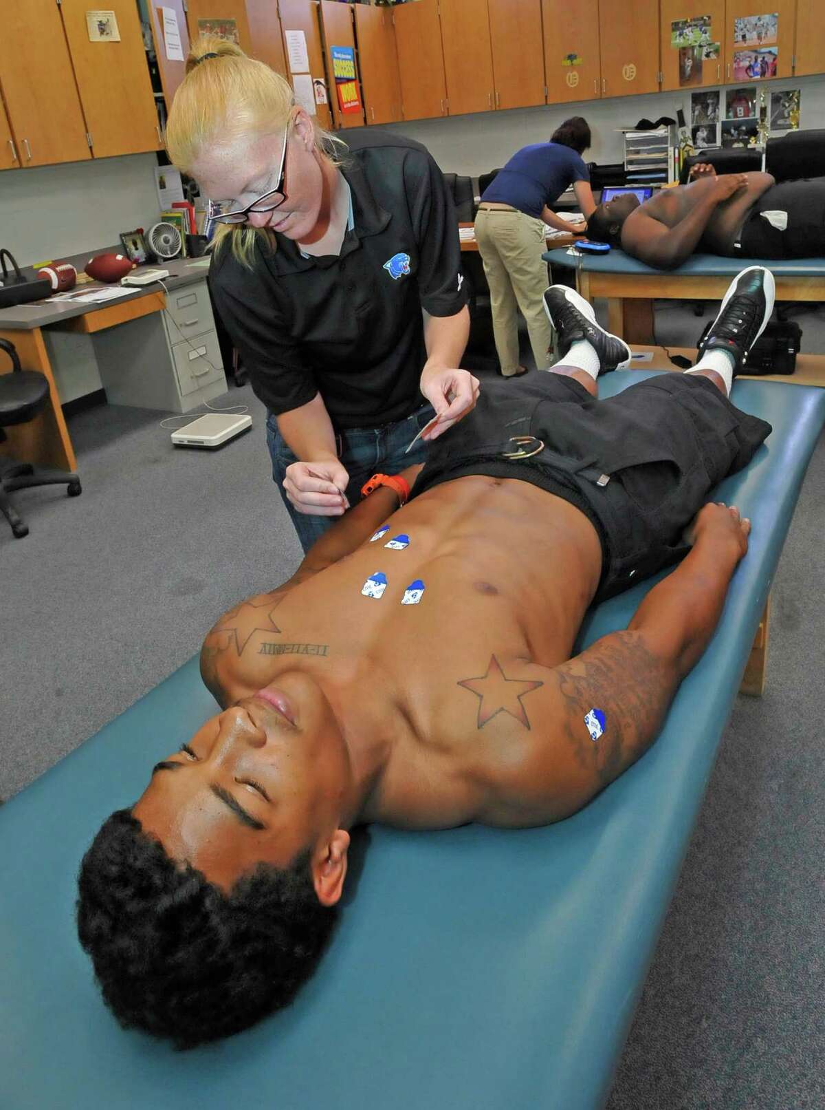 The coaches office was one of the sites used by Danae Tuhn, left, the Ozen Trainer, and Mary DeBauche, back, the Director of Operations for Cypress ECG as the two each hooked up one athlete at a time to the EKG transmitters that sent information to a computer. Tuhn was busy hooking up Ronnie Ceasar. The Beaumont Independent School District provided EKGs for athletes at Ozen High School on Thursday at the field house. The screenings are the result of a $15,000 grant and will check athletes for heart problems. The screenings will also take place at Central High School on Friday and West Brook High School on Monday. Dave Ryan/The Enterprise