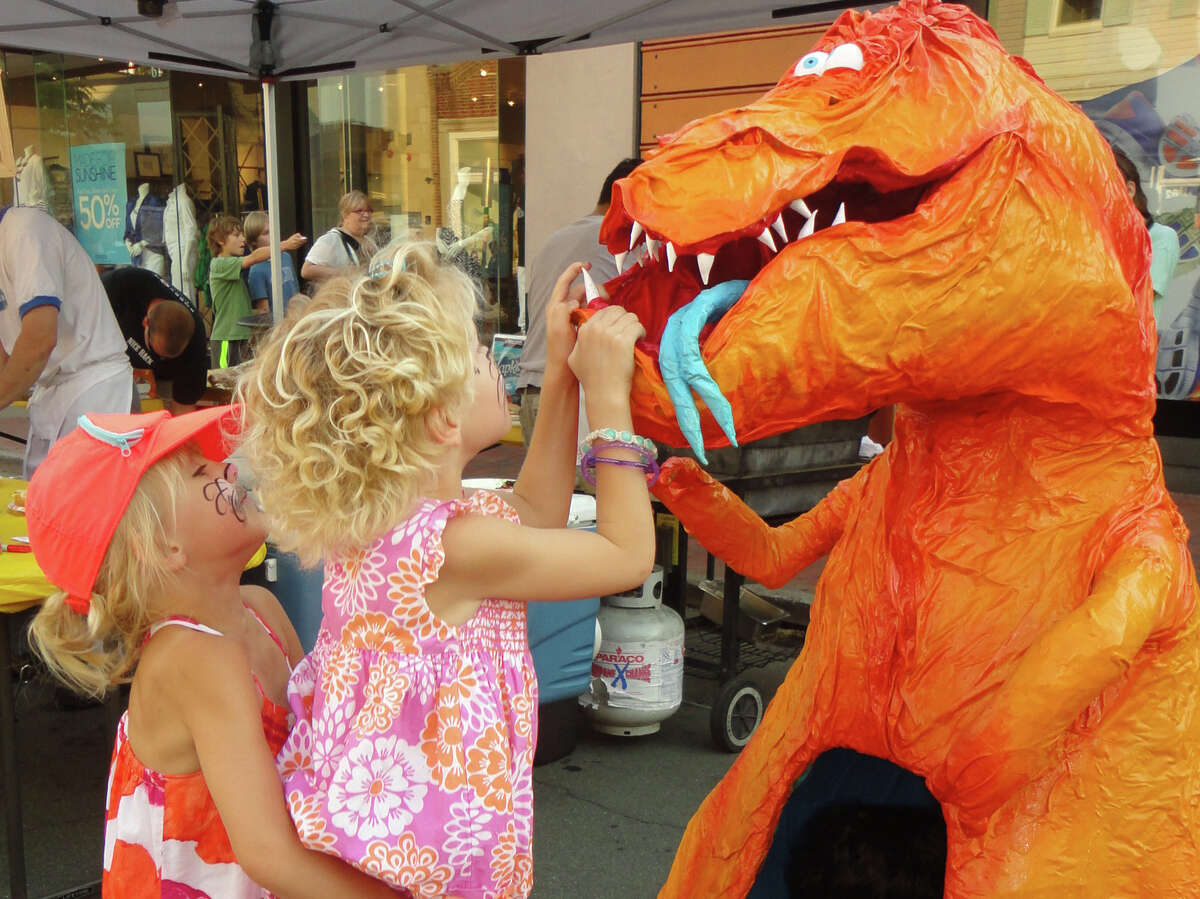 Cameron Cooleen, 5, lifts her twin sister Caleigh to get a look into the mouth of the dragon sculpture on Main Street during Thursday's Art About Town street party, organized by the Downtown Merchants Association. Caleigh returned the favor for her sister, and both girls also sat inside the dragon.