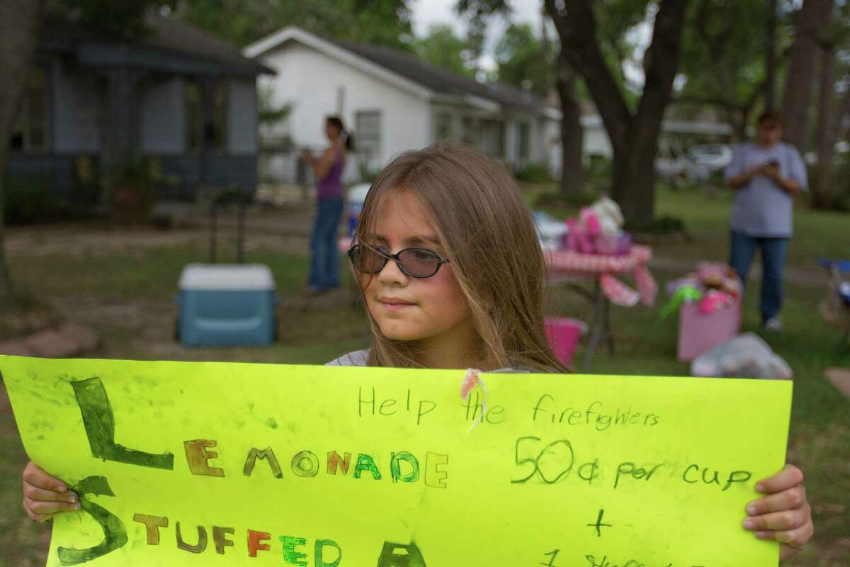 Cristina McInnis, 10, holds a sign for her lemonade stand in the Oak Forest neighborhood that she and a friend, Avery Brown, 7, organized to collect money to give to the local fire department after four fighters died in a 5-alarm fire Friday, Saturday, June 1, 2013, in Houston. The $185 donations went to their local fire stations, Station 13 and 31. "We heard about the firefighters so we wanted to help them because of their losses," she said.