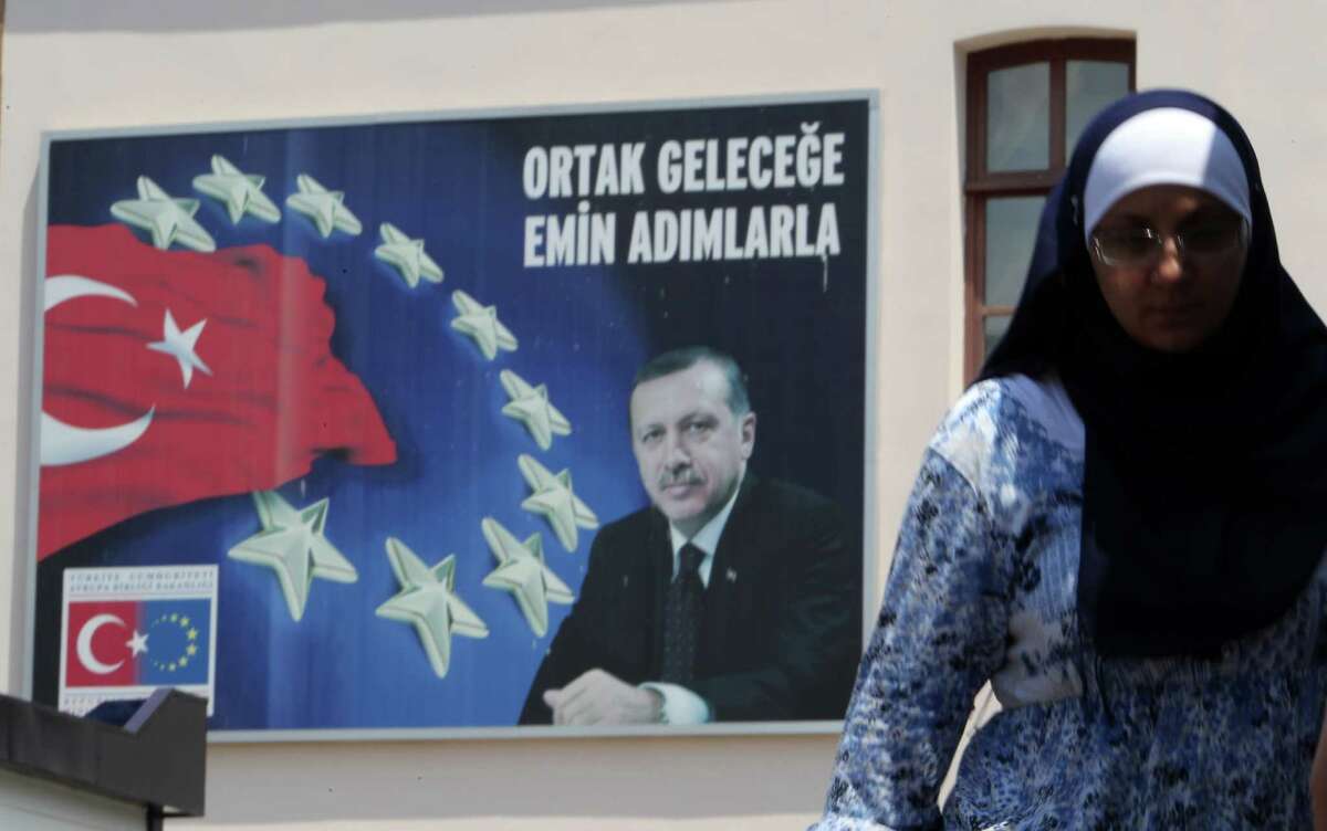 A woman walks next to a poster with a photo of Turkish Prime Minister, Recep Tayyip Erdogan, and the Turkish and European Union flags with the slogan ''Walking steadily to a joint future'' in Istanbul, Tuesday, June 4, 2013. Thousands have joined anti-government rallies across Turkey since Friday, when police launched a pre-dawn raid against a peaceful sit-in protesting plans to uproot trees in Istanbul's main Taksim Square. Since then, the demonstrations by mostly secular-minded Turks have spiraled into Turkey's biggest anti-government disturbances in years, and have spread to many of the biggest cities. (AP Photo/Thanassis Stavrakis)