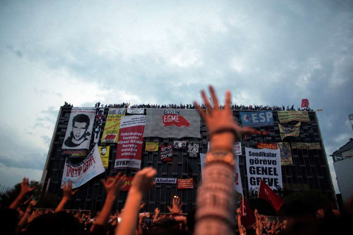 Protesters raise their hands and shout slogans in front of Ataturk Cultural center during a protest at Taksim square in Istanbul, Tuesday, June 4, 2013. One of the banners reads " the task of the trade unions stage a general strike" Thousands have joined anti-government rallies across Turkey since Friday, when police launched a pre-dawn raid against a peaceful sit-in protesting plans to uproot trees in Istanbul's main Taksim Square. Since then, the demonstrations by mostly secular-minded Turks have spiraled into Turkey's biggest anti-government disturbances in years, and have spread to many of the biggest cities. (AP Photo/Kostas Tsironis)