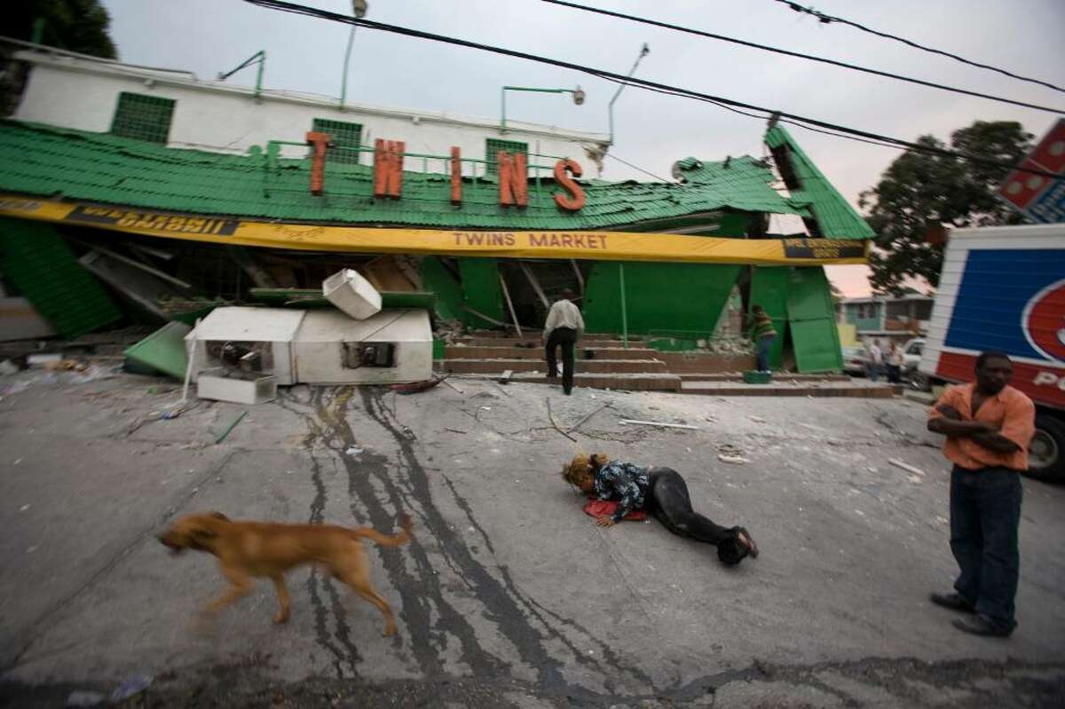 A woman lies on the ground as others stand outside a market that collapsed after a powerful earthquake struck Port-au-Prince, Haiti, Tuesday Jan. 12, 2010. (AP Photo/Cris Bierrenbach)