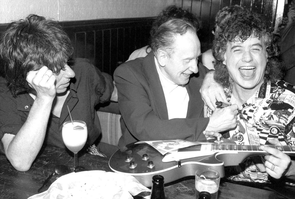 FILE - In this Nov. 6, 1987 file photo, guitar designer Les Paul, center, signs former Led Zeppelin guitarist Jimmy Page's chest after signing his guitar at a 72nd birthday party thrown for Paul by Gibson guitar company at New York's Hard Rock Cafe. Guitarist Jeff Beck, left, joined Paul and Page for the party, which drew a variety of rock music personalities. Les Paul was a renown musician also known for his innovations on the solid body electric guitar and multitrack recording. The man who helped pave the way for rock 'n' roll is finally getting a permanent exhibit on June 9, 2013 at the Waukesha County Museum in his Wisconsin hometown. (AP Photo/John Bellissimo, file)