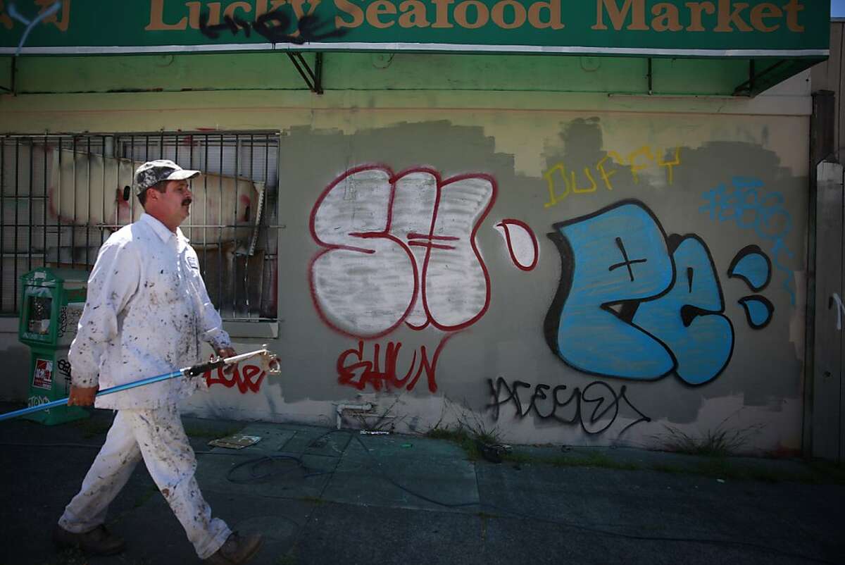 Hayward Blake, electrical painter with Keep Oakland Clean and Beautiful, carries a spray gun extension as he walks past graffiti along 12th Street before demonstrating how to paint over it on Wednesday, June 12, 2013 in Oakland, Calif.