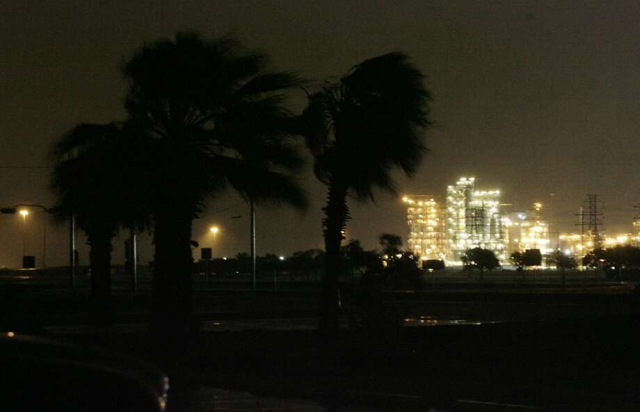 Palm trees along Highway 332 in Lake Jackson sway in the gusty winds from Hurricane Ike as the Dod Chemical Plant is seen hours before landfall on Friday, Sept. 12, 2008, in Surfside Beach. While all of Lake Jackson was in the dark because of power outages, the Dow Chemical Plant remained lit thanks to generators. ( Julio Cortez / Chronicle )
