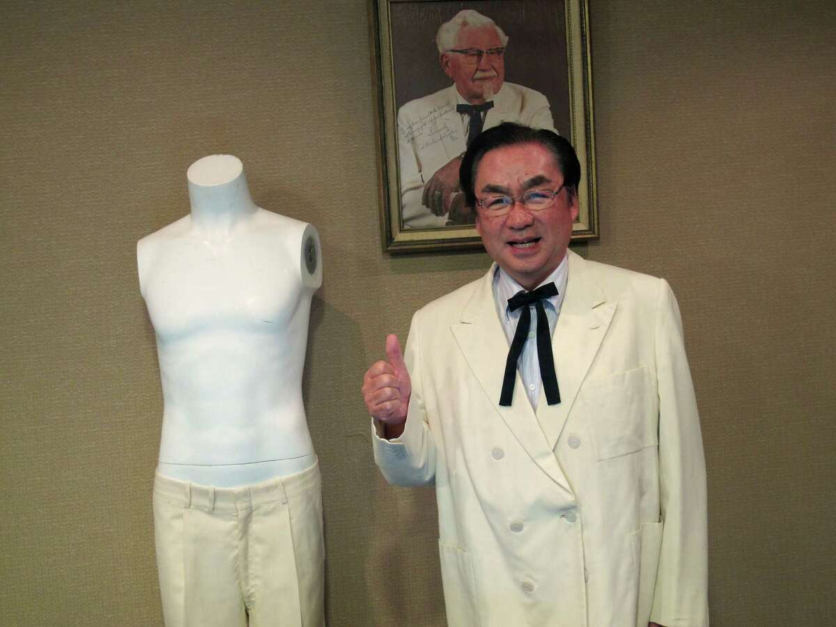Masao "Charlie" Watanabe, president and chief executive of Kentucky Fried Chicken Japan, stands beneath a portrait of company founder "Colonel" Harland Sanders on Saturday, June 22, 2013, at Heritage Auctions in Dallas. Watanabe is wearing Sanders' trademark white suit jacket and black string tie after he purchased them at the auction, which featured other items, including leg irons that restrained abolitionist John Brown. (AP Photo/Angela K. Brown)