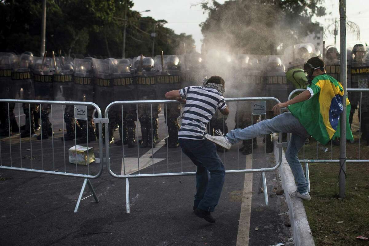 A protester trying to open a barrier, left, is kicked by another protester asking for peace near a police line as they protest outside Minerao stadium where a Confederations Cup soccer match takes place between Japan and Mexico in Belo Horizonte, Brazil, Saturday, June 22, 2013. Demonstrators once again took to the streets of Brazil on Saturday, continuing a wave of protests that have shaken the nation and pushed the government to promise a crackdown on corruption and greater spending on social services. (AP Photo/Felipe Dana)
