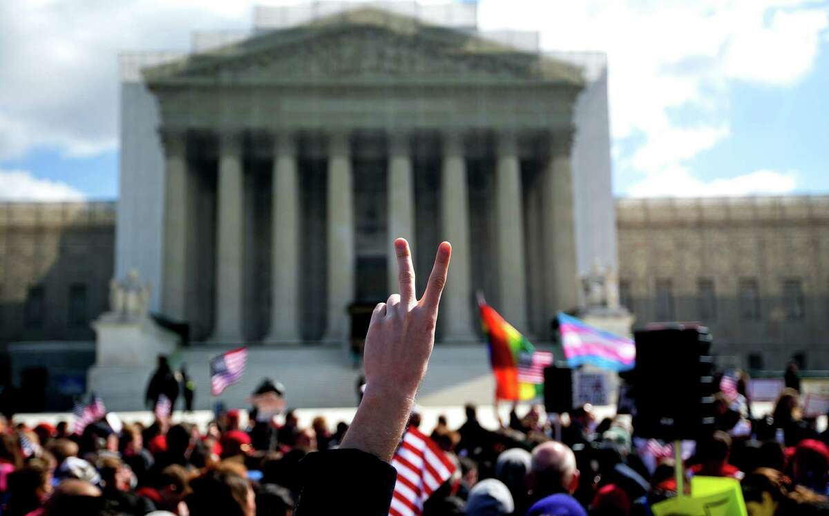 A demonstrator holds up a victory sign with other protesters in support of and opposed to same-sex marriage, outside the U.S. Supreme Court in Washington, March 27, 2013. The court returns to the subject of same-sex marriage for a second day Wednesday, when the justices hear arguments about the constitutionality of the federal Defense of Marriage Act of 1996. (Doug Mills/The New York Times)