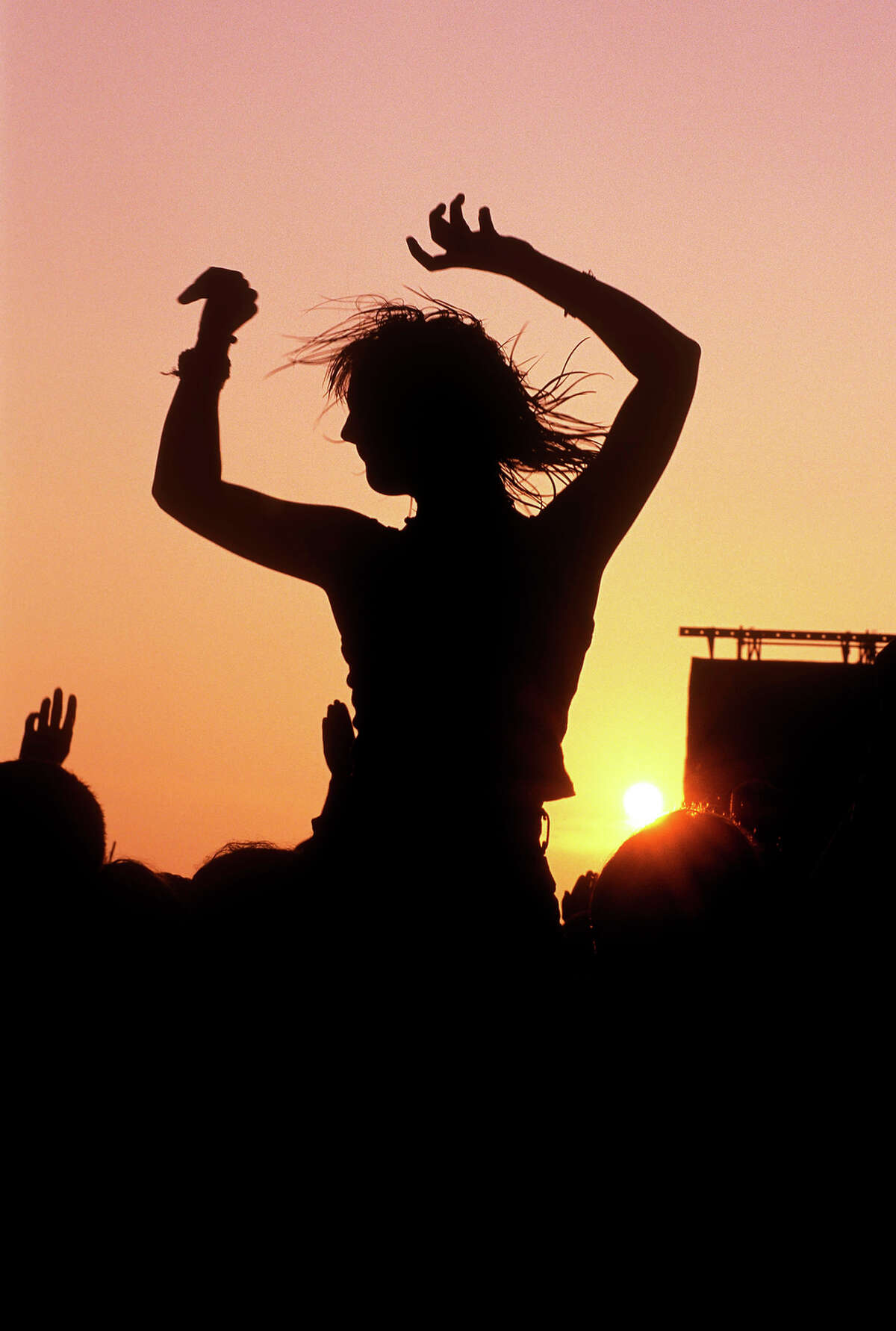 1970: A woman sitting on shoulders above crowds at sunset at Glastonbury Festival.